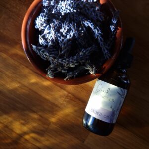 Organic lavender oil in amber colored dropper bottle on oak wood, next to a bowl of organic lvender buds.