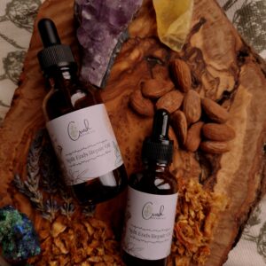 Two bottles of Split Ends Hair repair Oil surrounded by herbs, ingredients and crystals on a wooden board